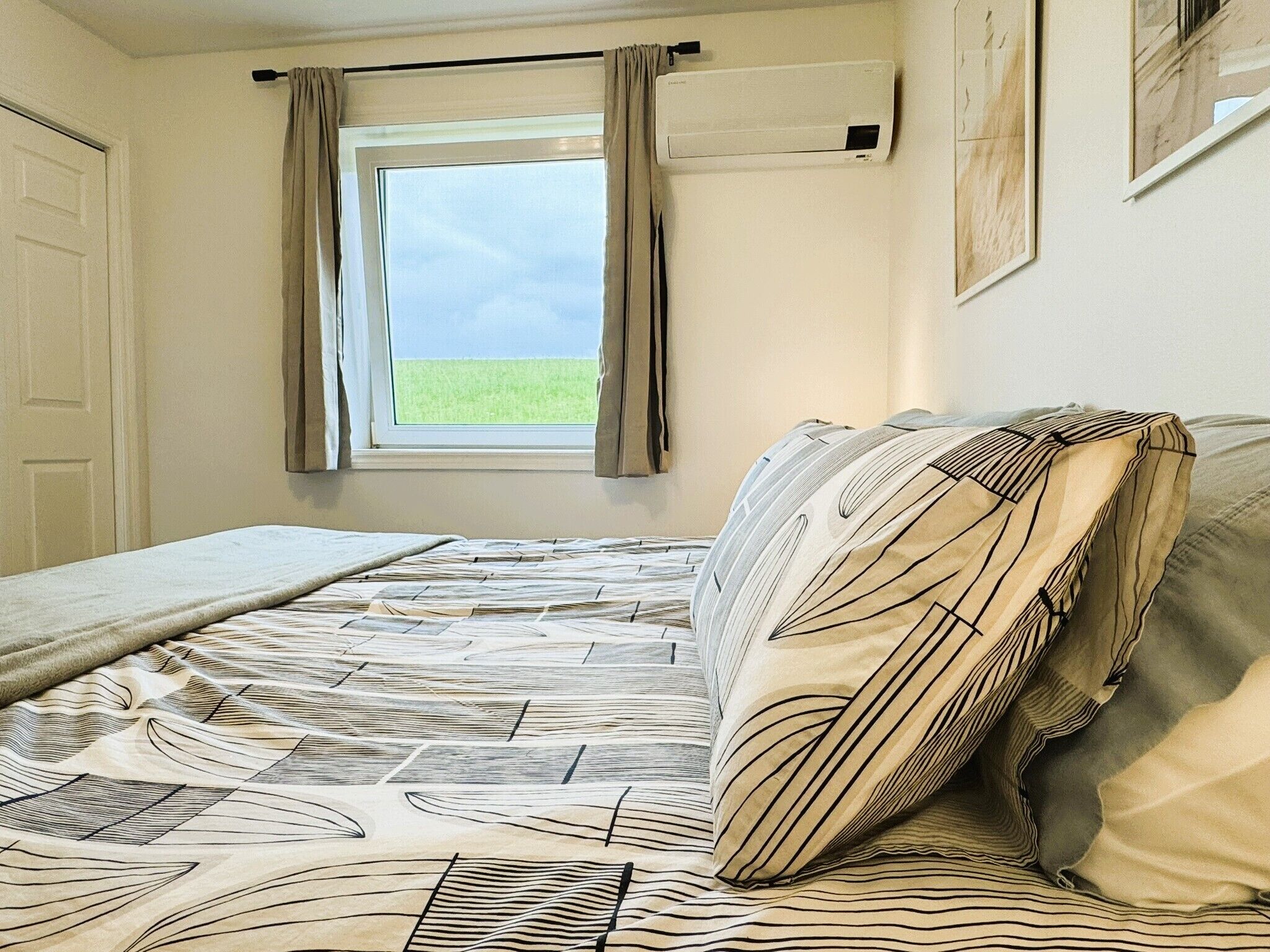Een slaapkamer met een bed, een raam met gordijnen en een wandairconditioner.