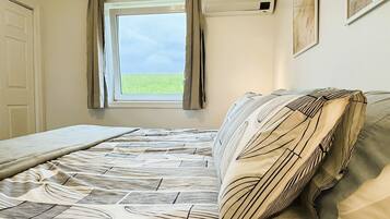 Een slaapkamer met een bed, een raam met gordijnen en een wandairconditioner.
