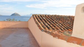 A rooftop terrace with terracotta tiles, a view of the sea, and a distant island.