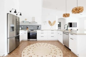 A modern kitchen with stainless steel appliances, white cabinetry, a patterned backsplash, and decorative wall art.