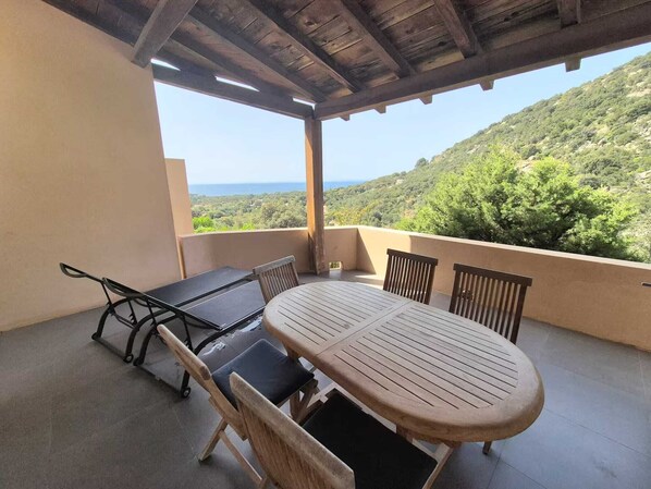 A covered outdoor patio with a table and chairs, overlooking a hilly landscape.