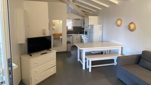 A modern living room with a flat-screen TV, a sofa, a dining table, and a kitchen in the background.