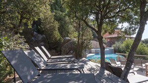 A wooden deck with lounge chairs and a pool area, surrounded by trees and rocks.