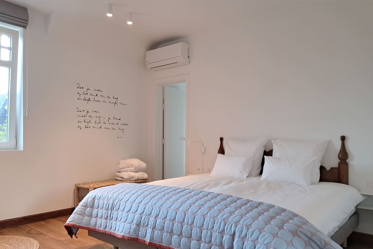 Une chambre à coucher comprenant un lit, une table de chevet, un climatiseur fixé au mur et une fenêtre.