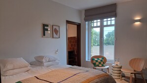 Un dormitorio con cama, una silla, una mesita, un ventanal y una pared de ladrillo.