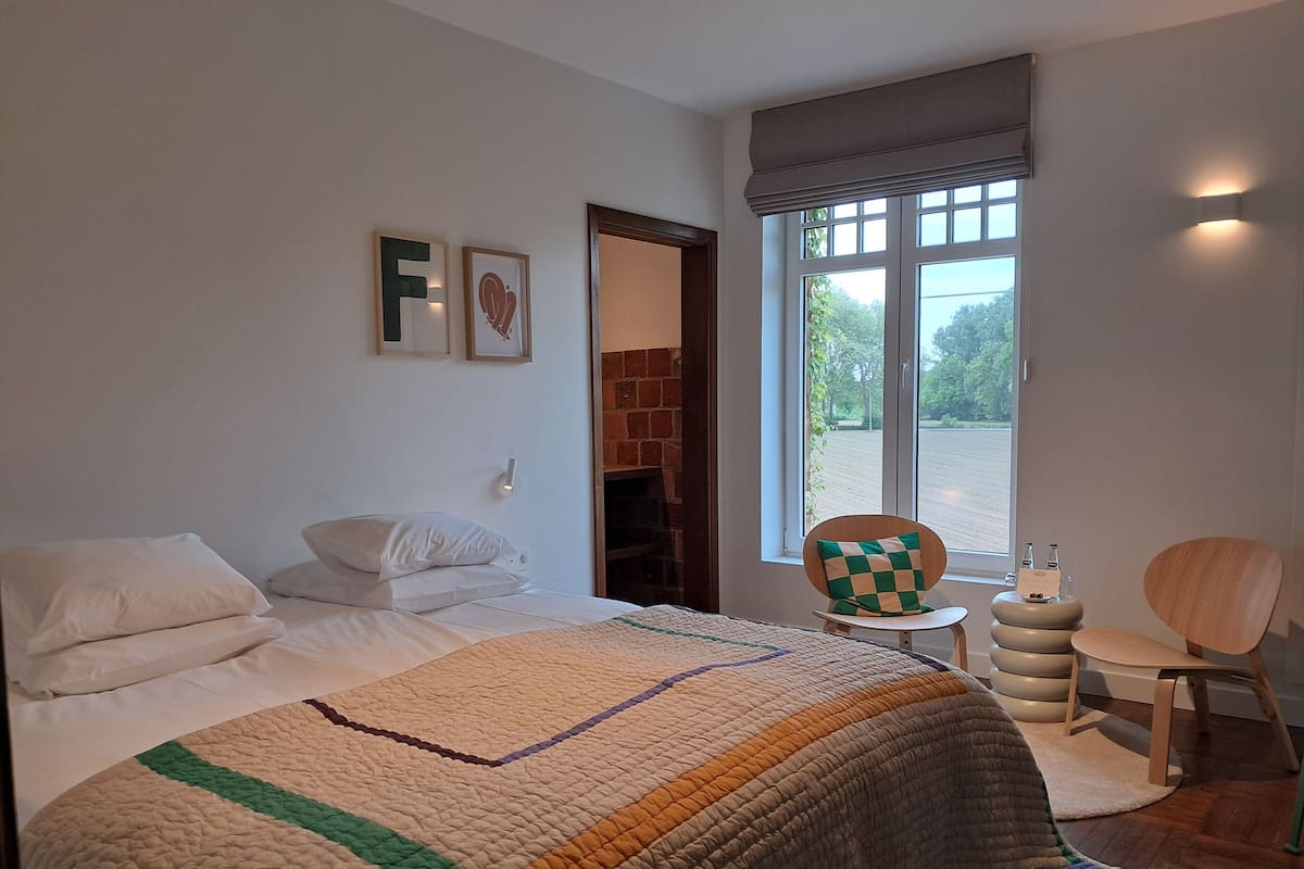 Une chambre à coucher avec un lit, une chaise, une petite table, une fenêtre et un mur en briques.