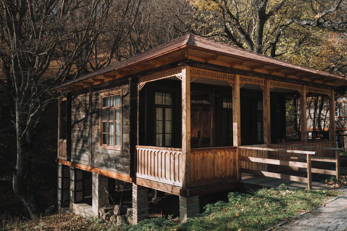 Una cabaña de madera rústica con un porche, rodeada de árboles.