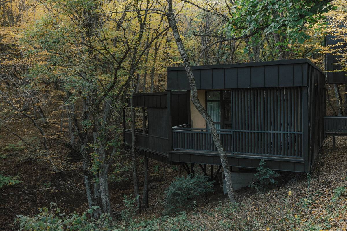 Una cabaña en un bosque con un balcón y una ventana.