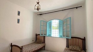 Ein Zimmer mit zwei Einzelbetten, einem Fenster mit blauen Fensterläden, einer Kristallleuchtre und fugenwerkgefliester Boden.