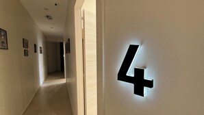 Corredor com um número '4' iluminado na parede, que leva a um quarto.
