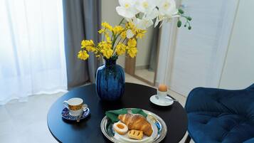 Ett matbord med en blå vas fylld med gula och vita blommor, en tallrik med croissanter och en kopp kaffe, samt en blå stol.