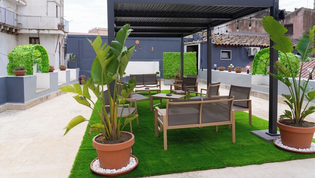 Un patio en la azotea con un área de descanso techada, césped artificial verde y plantas en macetas.