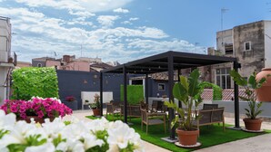 Una terraza en la azotea con pérgola, zona de estar y plantas en macetas.