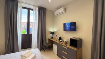 Habitación de hotel con cama, escritorio, silla, televisor y aire acondicionado.