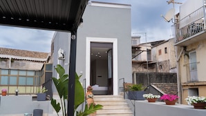 Um edifício moderno com fachada cinzenta, entrada visível e escadaria que leva a um andar superior.