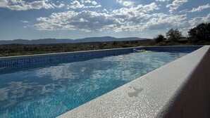 A swimming pool with clear blue water, surrounded by a tiled edge, and a view of distant mountains under a partly cloudy sky. - Romantic Wine Country Retreat • Private Hot Tub & Valley Views (Cornville)