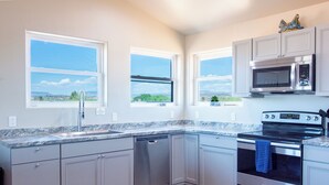 A modern kitchen with grey cabinets, stainless steel appliances, a dishwasher, and a view of the city through large windows. - Romantic Wine Country Retreat • Private Hot Tub & Valley Views (Cornville)