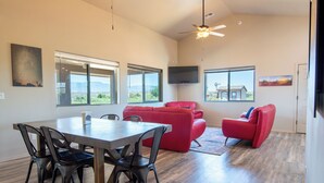 A spacious living area with a dining table, red sofas, and a flat-screen TV mounted on the wall. - Romantic Wine Country Retreat • Private Hot Tub & Valley Views (Cornville)