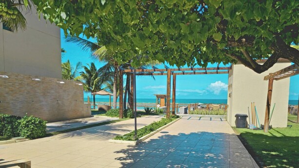 Un camino que lleva a una playa con palmeras, una pérgola de madera y vista al océano.