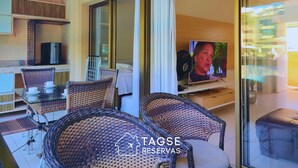 Habitación con mobiliario de mimbre, un televisor y vistas a una piscina y un edificio.