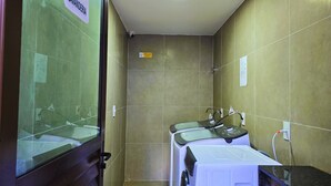 A small, enclosed bathroom with a shower, a sink, and a mirror. There is a sign indicating the location of the bathroom.