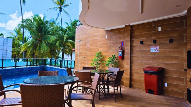 A poolside area with wicker chairs and a table, a red trash bin, and a sign prohibiting smoking.