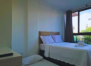 Quarto de hotel com cama, mesa de cabeceira e janela com cortinas.