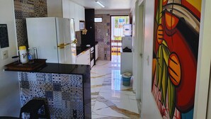 A modern kitchen with white cabinets, a marble floor, and a colorful mural on the wall. - POR012 | 3-Suite Apartment in Porto de Galinhas (Ipojuca)