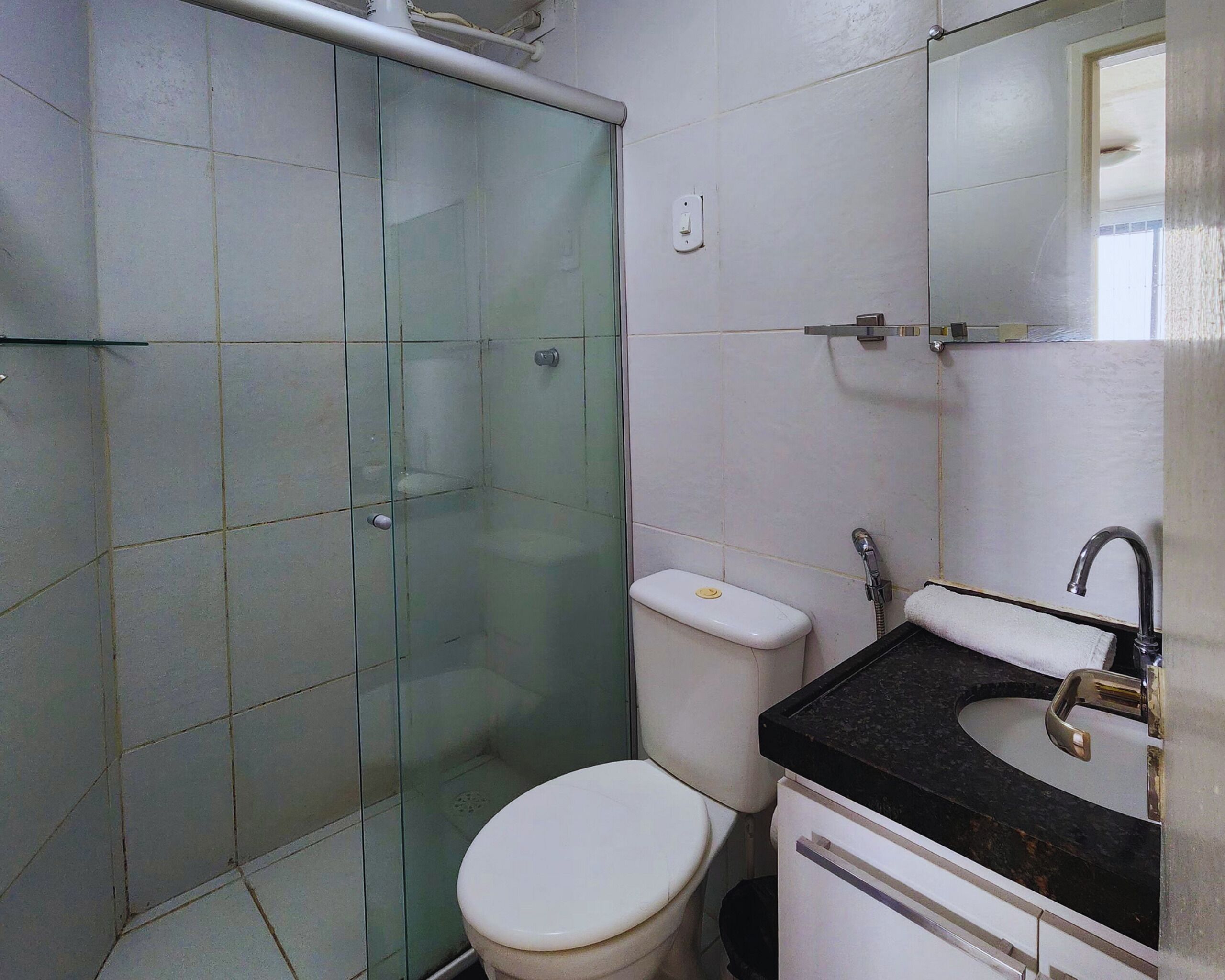 Een badkamer met een douche met glazen wand, een wit toilet en een wastafel met een zwart aanrecht.