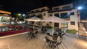 An outdoor patio with tables and chairs, umbrellas, and a swimming pool. - POR012 | 3-Suite Apartment in Porto de Galinhas (Ipojuca)