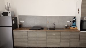 A modern kitchen with grey cabinets, a stainless steel refrigerator, a microwave, a coffee machine, and an oven.