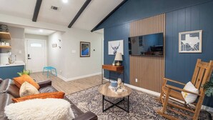 Un salon avec un mur d’accent de couleur bleu foncé, une table basse en bois, un canapé en cuir et un fauteuil à bascule.