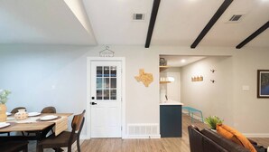 Un coin repas avec une table et des chaises en bois, une porte blanche avec un panneau en verre et une décoration murale sur le thème du Texas.