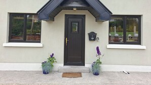 Une maison avec une porte d’entrée de couleur sombre, deux fenêtres à encadrements sombres et un petit porche avec des marches.