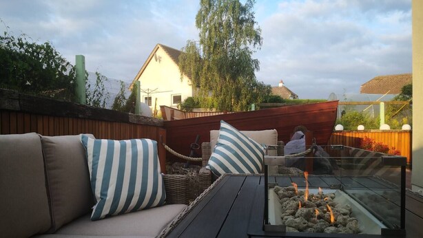 Une terrasse avec un canapé, des coussins et une table en verre dotée d’un foyer intégré.