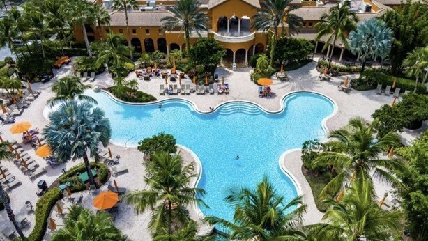 An aerial view of a resort with a large pool, palm trees, and a building with a yellow facade. - 3Bedroom 2.5 bath townhome in beautiful Naples Florida

: (Naples)