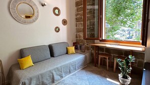 A cozy room with a grey sofa, yellow cushions, a round mirror, and a window with a view of greenery. - ALGHERO CENTER LOFT MARIS IN SULIS SQUARE: ICONIC WATERFRONT LOFT-TOP LOCATION (Alghero)