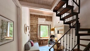A cozy living room with a stone wall, a wooden staircase, and a comfortable seating area. - ALGHERO CENTER LOFT MARIS IN SULIS SQUARE: ICONIC WATERFRONT LOFT-TOP LOCATION (Alghero)
