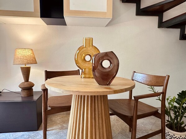 A round wooden table with a textured lamp, a decorative vase, and a chair.