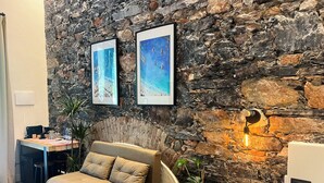 A cozy room with a stone wall, a sofa, a small table, and a potted plant. - La Campanula (La Spezia)