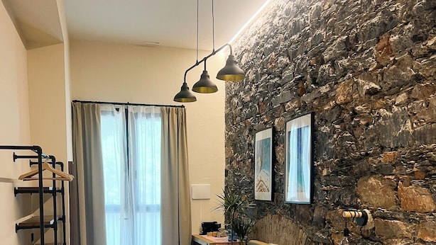A modern bedroom with a stone wall, a bed with towels, a sofa, and a desk with a coffee machine. - La Campanula (La Spezia)