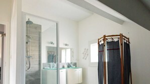 Un dormitorio con una cama grande, cabina de ducha de vidrio, estructura de cama con dosel de madera, y un baño con espejo y lavamanos.