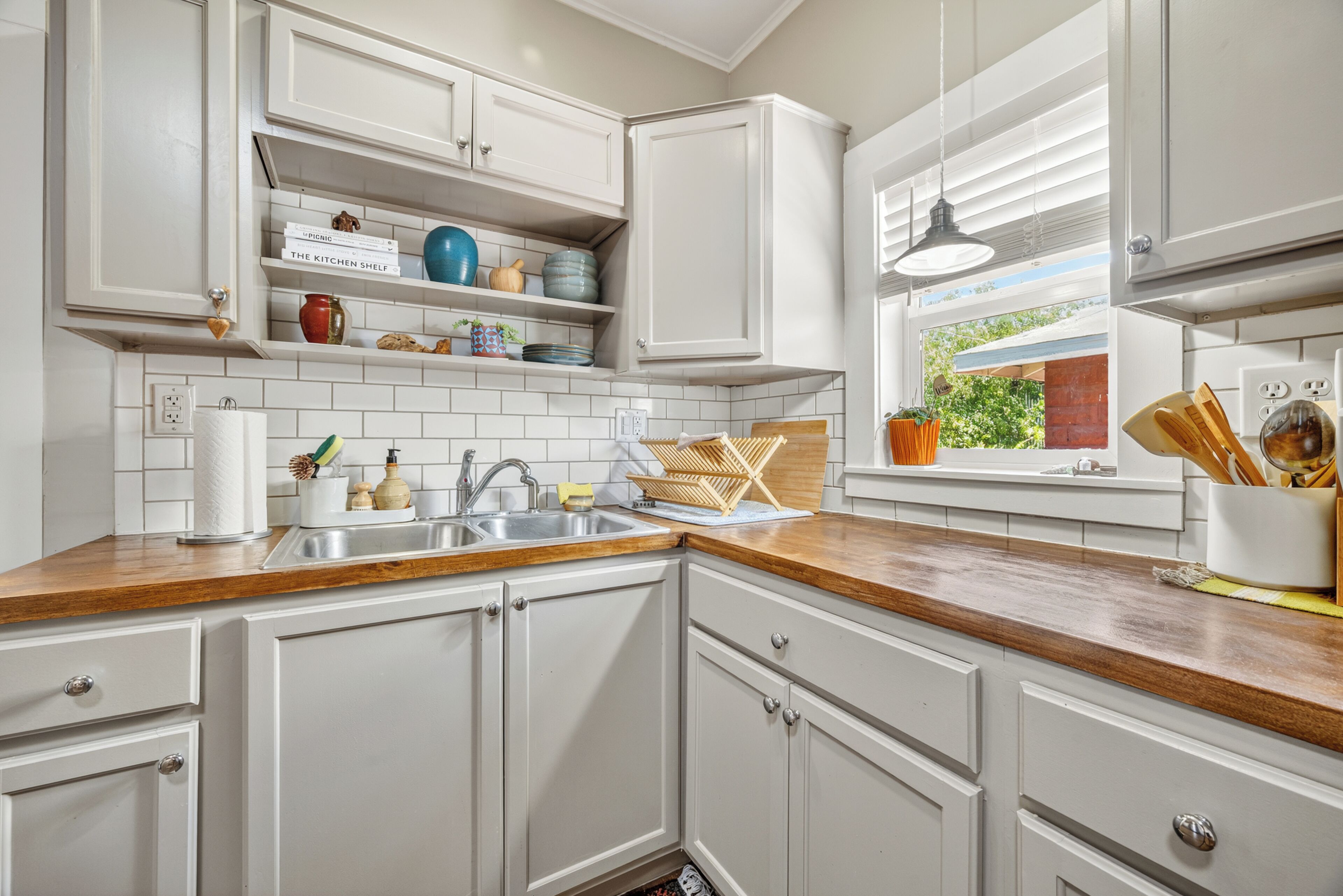 A kitchen with white cabinetry, a wooden countertop, a built-in sink, and a window with blinds.