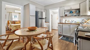 A modern kitchen with white cabinets, a stainless steel refrigerator, and a dining area with a wooden table and chairs.