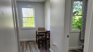 A hallway with wooden flooring, a dining table with chairs, and a window with a view of greenery. - Ninth Door Mention Apt 13 Main St. Milbridge (Milbridge)