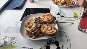 Una mesa con comida que incluye pasta, panecillos y una bebida.