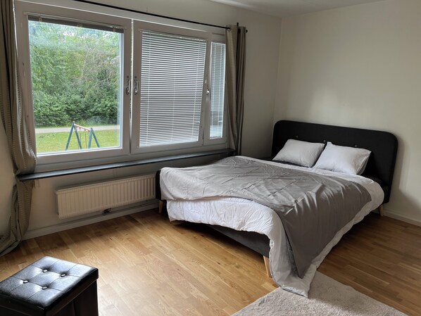 Une chambre à coucher avec un lit, une fenêtre avec des stores, un radiateur et un plancher en bois.