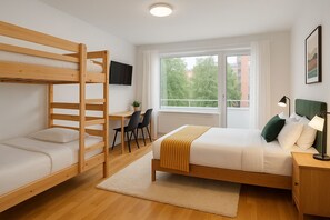 Une chambre avec un lit superposé, un bureau avec deux chaises, un lit avec une tête de lit verte, une lampe de chevet et une fenêtre donnant sur des arbres et des bâtiments.
