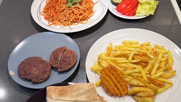 Ein Tisch mit verschiedenen Speisen, darunter Spaghetti, Pommes, Fladenbrote und eine Gemüseplatte.