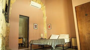 A bedroom with a bed, a wooden door, an air conditioning unit, and a mirror.